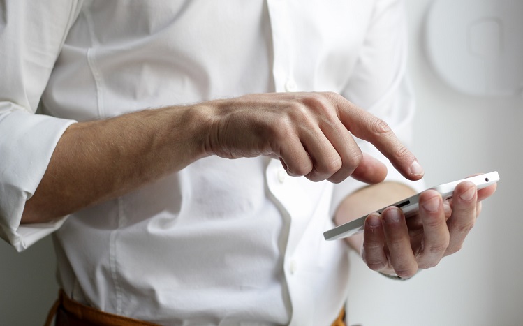 un homme en chemise blanche touche du doigt l'écran de son téléphone portable - nordwood-themes-unsplash
